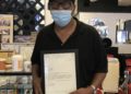 A masked black man holds a framed letter in a barbershop