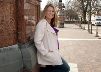 woman leaning against a brick wall in a white jacket