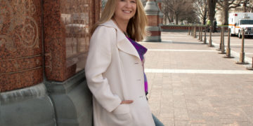 woman leaning against a brick wall in a white jacket