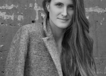 A woman with long hair looking at the camera wearing a coat