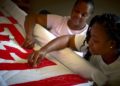 two black women bent over a quilt with a red pattern