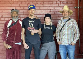 group of four people standing against a red brick wall